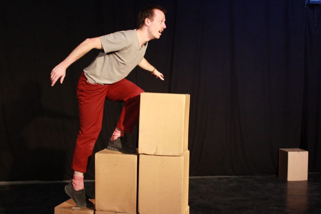 Ein Playbacktheater-Schauspieler steigt auf einen Turm Kartons im Theater.